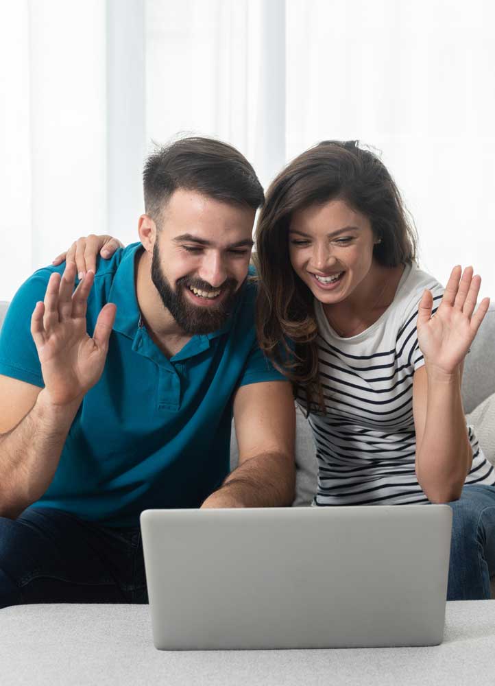 Young couple sitting in their living room with laptop waving to their marital therapist after successful online therapy and saved marriage