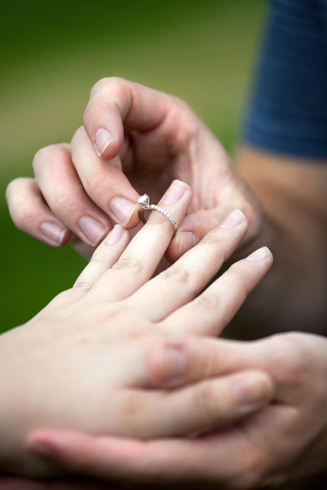 Man placing a diamond engagement ring on the finger of his fiance. Shallow depth of field with focus on the ring.